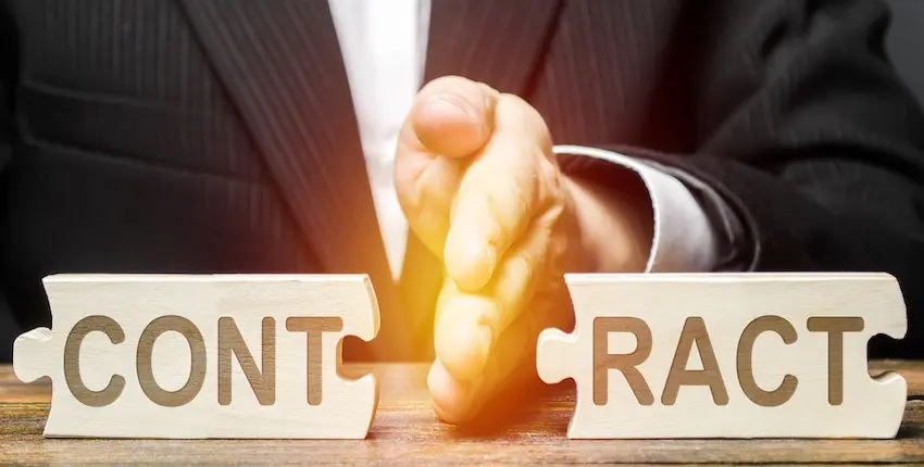 A lawyer- from Rosenbaum & Taylor P.C.- in a dark pinstriped business suit drives the blade of their hand downward between two interlocking wooden puzzle pieces engraved with the letters CONT on the left piece and RACT on the right forcibly splitting them apart on a wooden table surface with a warm orange glow emanating from the point of separation — a striking visual metaphor for the deliberate severing of a legal agreement and the moment a material breach occurs in New York.